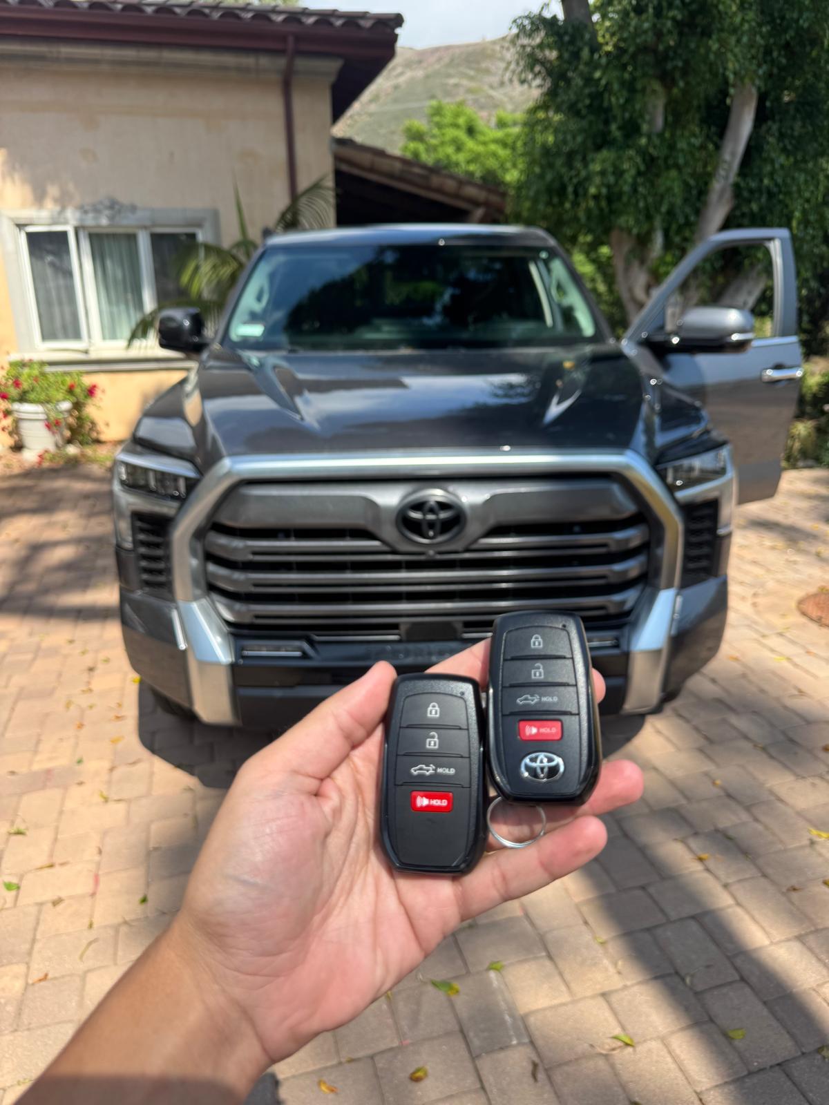 Two Toyota key fobs photographed in front of a pickup